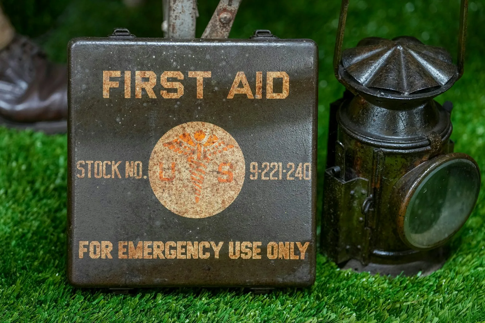 A vintage metal first aid box beside a lantern on grass