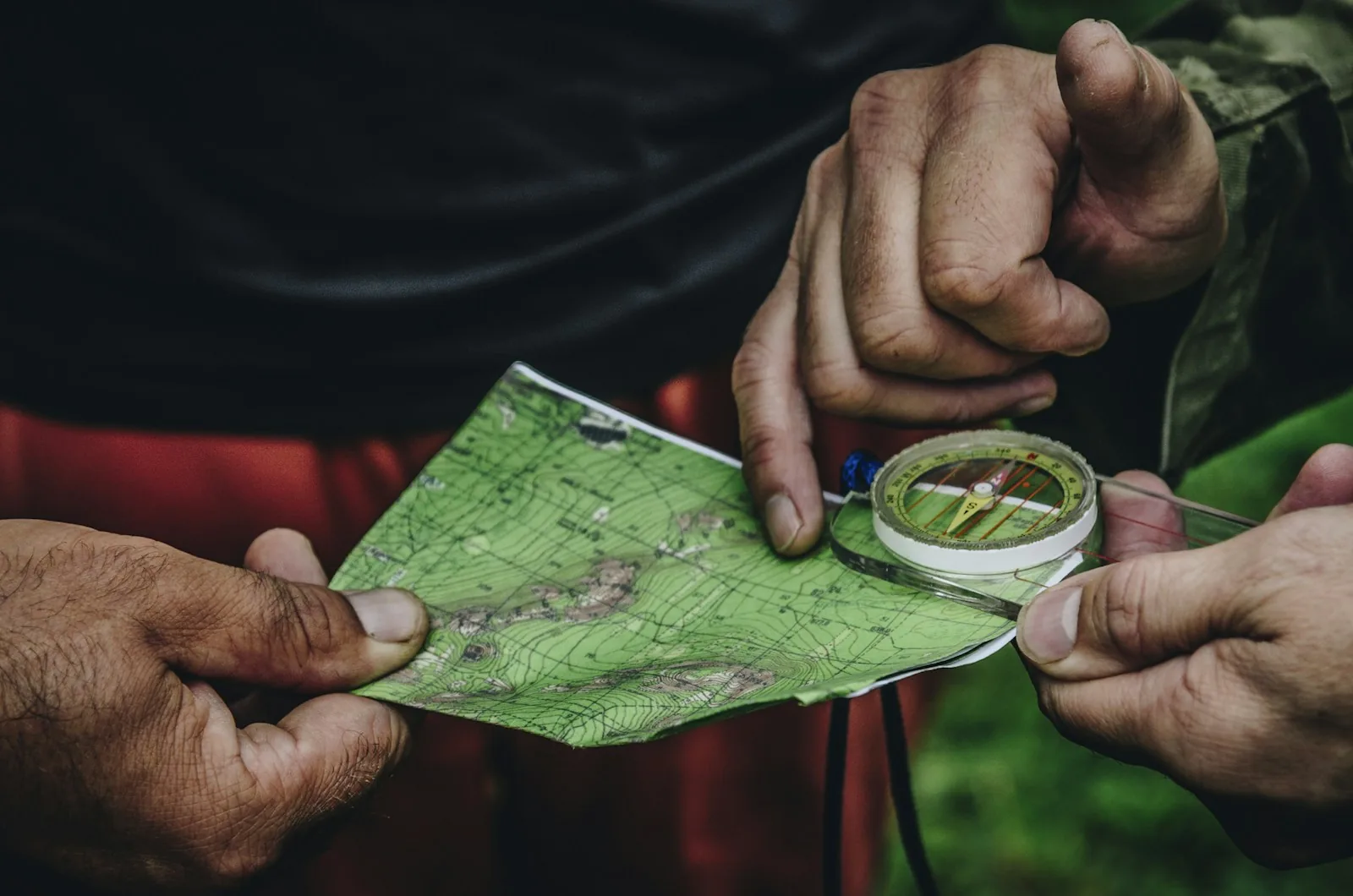 Hands checking a baseplate compass against a folded topographic map