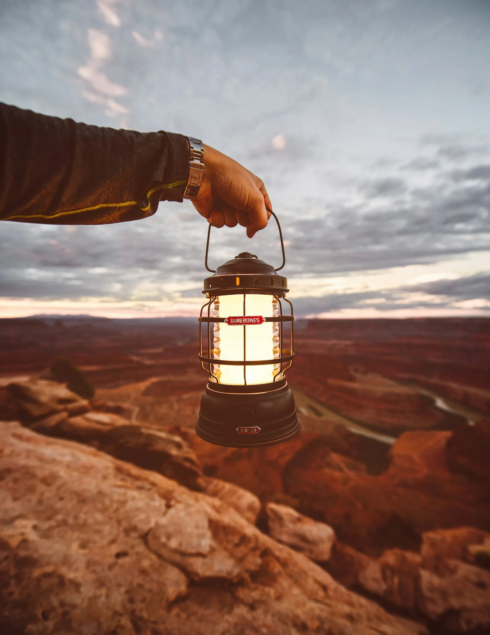 A hand holding an illuminated portable lantern outdoors at dusk